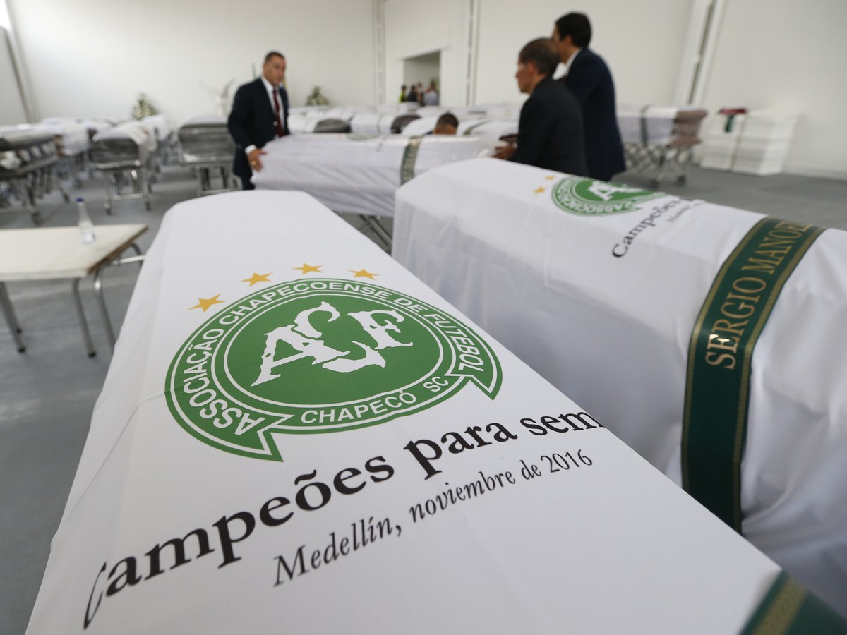 Zamestnanci pohrebnej služby zakrývajú rakvy bielymi prikrývkami s logom brazílskeho futbalového tímu Chapecoense