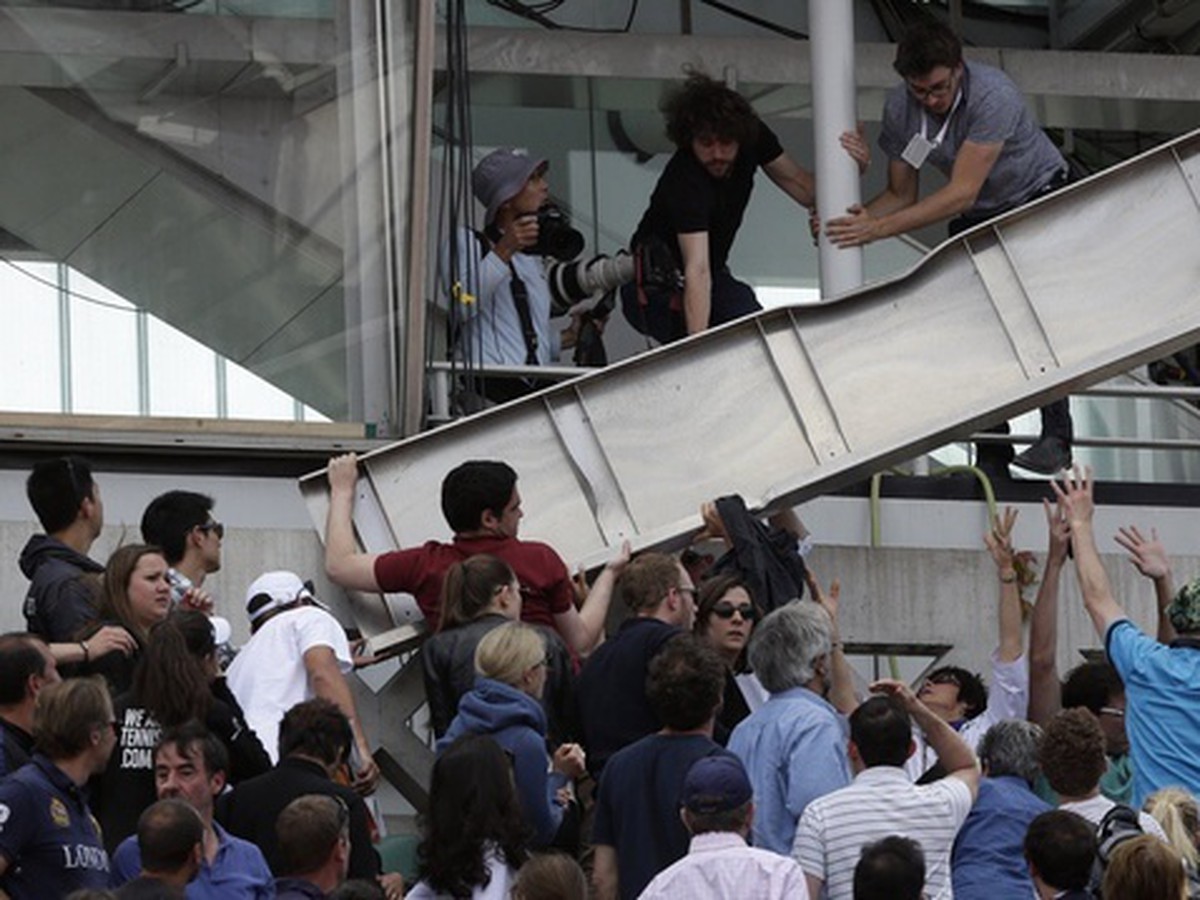 Ľudia odnášajú časť panelu, ktorý spadol na stánok na centrálnom kurte počas štvrťfinálového zápasu medzi Japoncom Keiom Nišikorim proti Francúzovi Jo-Wilfriedovi Tsongovi