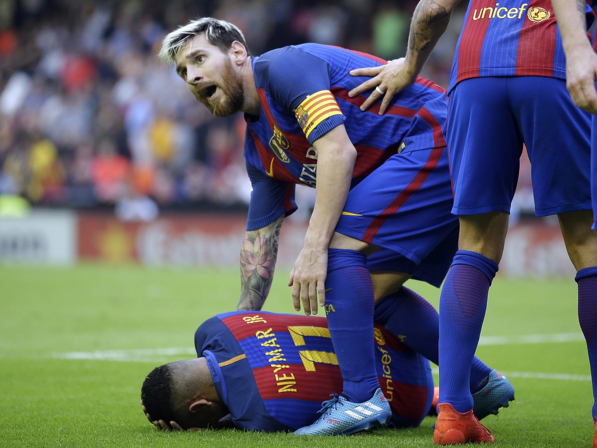 Futbalista FC Barcelona Lionel Messi stojí nad spoluhráčom Neymarom, ktorý leží na trávniku po tom, čo diváci začali hádzať predmety do futbalistov Barcelony 