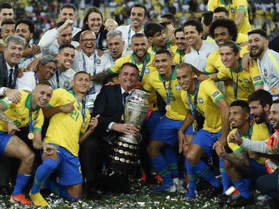 Brazílsky prezident Jair Bolsonaro drží trofej, keď oslavuje s brazílskymi hráčmi výhru nad Peru