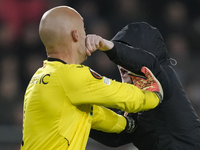Brankár Marko Dmitrovič zo Sevilly dostáva úder do tváre od fanúšika PSV v odvetnom zápase play off o osemifinále Európskej ligy