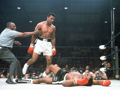 americký šampión v boxe ťažkej váhy Muhammad Ali (v strede) stojí vedľa rozhodcu Joa Walcotta (vľavo) po tom, ako knokautoval svojho súpera Sonnyho Listona