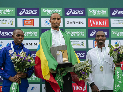 Mulugeta Uma oslavuje výhru v Parížskom maratóne, vedľa neho na pódiu Titus Ekiru a Elisha Rotich
