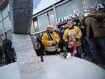 Fanúšikovia stoja pred pamätníkom zosnulému hokejistovi Pavlovi Demitrovi, ktorý je vytesaný do kameňa a má formu čepele a hokejky s pukom pred hlavným vchodom ZŠ Pavla Demitru v Trenčíne