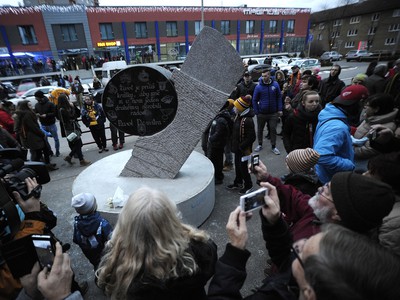 Fanúšikovia stoja pred pamätníkom zosnulému hokejistovi Pavlovi Demitrovi, ktorý je vytesaný do kameňa a má formu čepele a hokejky s pukom pred hlavným vchodom ZŠ Pavla Demitru