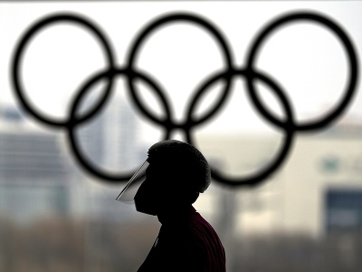 Osoba s ochranným štítom na tvári kráča okolo olympijských kruhov v novinárskom tlačovom centre na zimné olympijské hry 2022 v Pekingu 