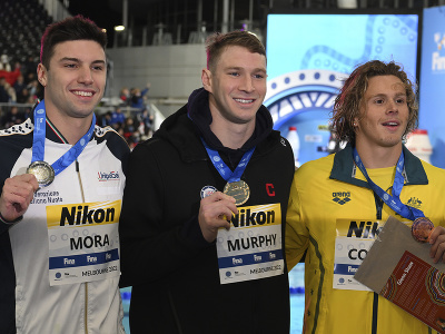 Víťazný americký plavec Ryan Murphy (uprostred) oslavuje na pódiu s druhým Talianom Lorenzom Morom (vľavo) a tretím Austrálčanom Isaacom Alanom Cooperom (vpravo) po finále na 100 m znak na MS v krátkom bazéne v austrálskom Melbourne