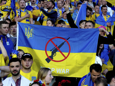Ukrajinskí fanúšikovia držia ukrajinskú vlajku s preškrtnutou zbraňou a nápisom 