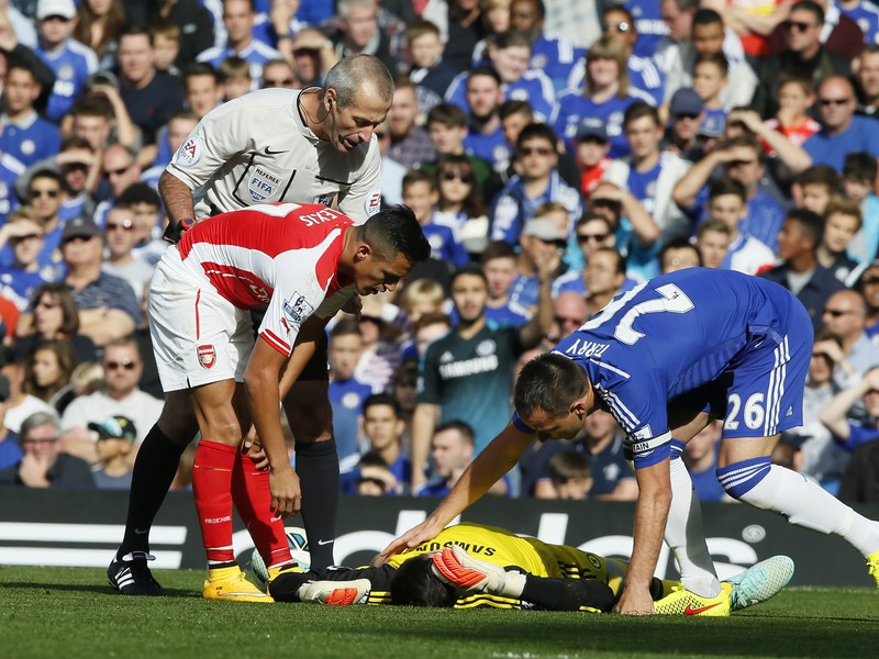 Alexis Sánchez po kolízii s brankárom Courtoisom, vpravo John Terry
