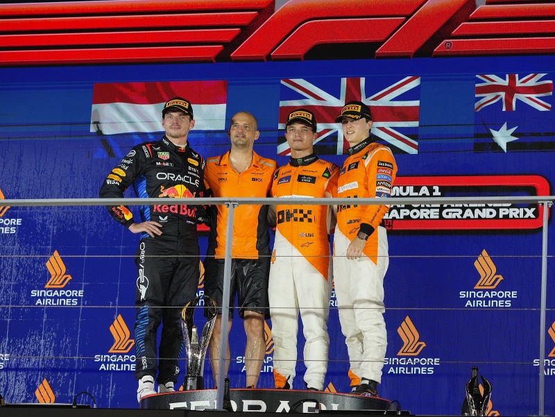 Stupeň víťazov VC Singapuru - zľava Max Verstappen, Lando Norris po boku člena tímu McLaren, a celkom vľavo Oscar Piastri