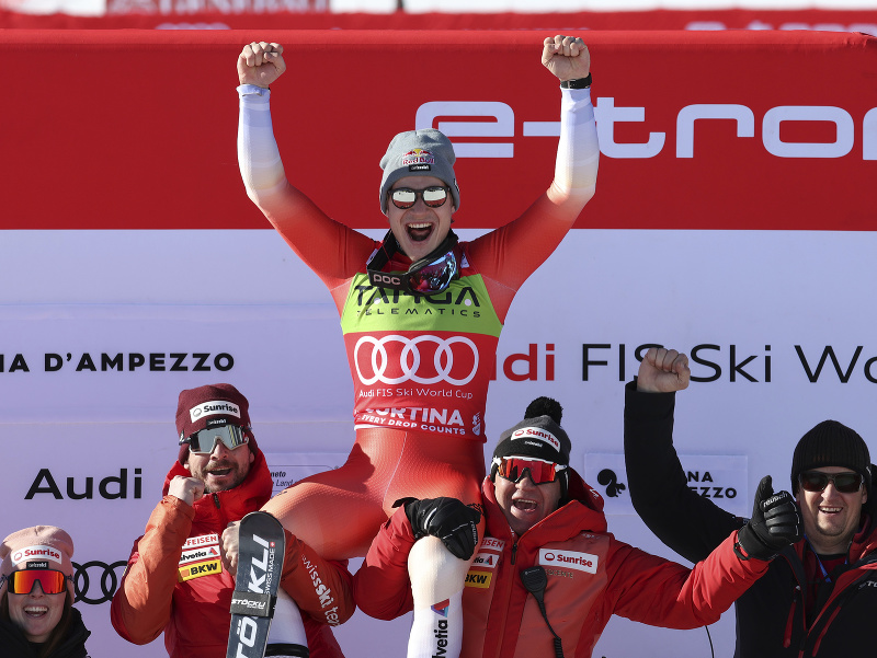 Švajčiarsky lyžiar Marco Odermatt (hore uprostred) oslavuje na pódiu so svojím tímom