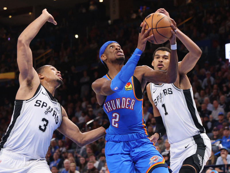 Shai Gilgeous-Alexander (2) proti brániacim hráčom San Antonia Keldonovi Johnsonovi (3) Victorovi Wembanyamovi