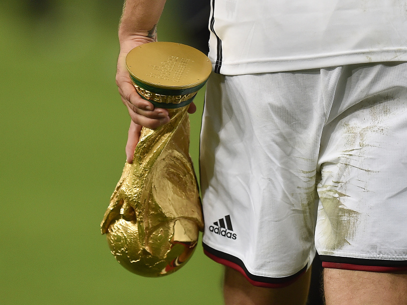 Nemecký futbalový reprezentant Lukas Podolski odchádza z trávnika s trofejou pre víťaza majstrovsiev sveta vo futbale oblečený v drese značky Adidas 