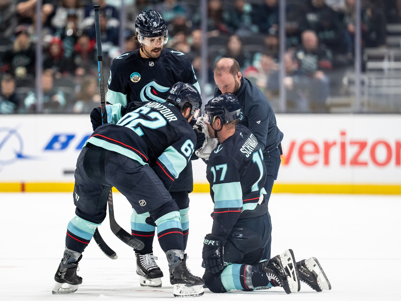 okejový útočník Jaden Schwartz zo Seattlu Kraken (17) po zásahu korčuľou, pomáhajú mu spoluhráči Brandon Montour (62) a Chandler Stephenson (9) 