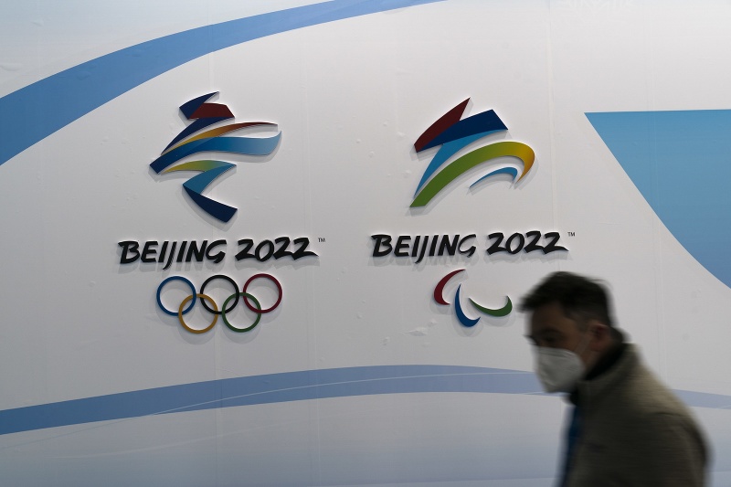 Muž s respirátorom KN95 kráča okolo olympijského loga pred začiatkom ZOH
