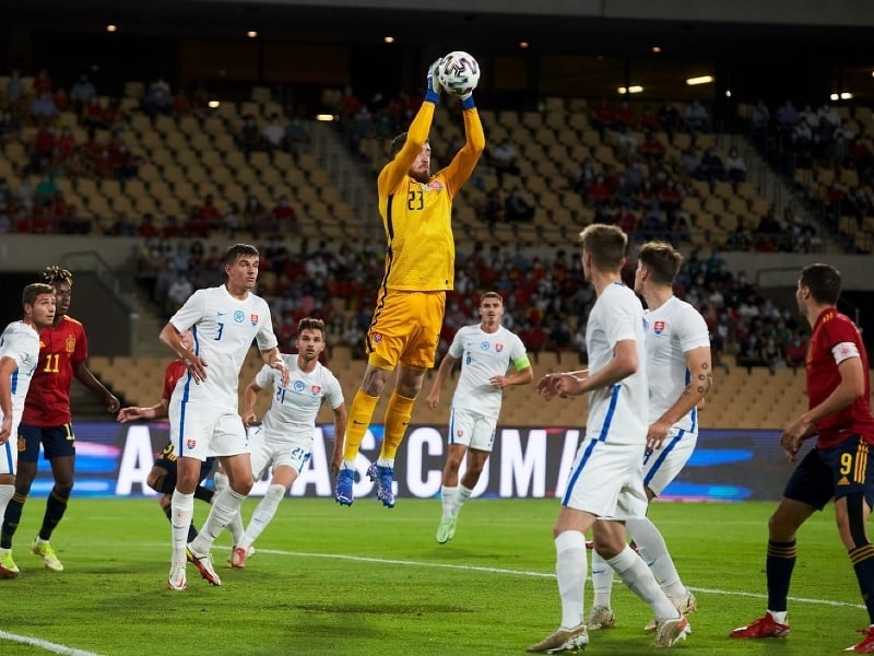 Brankár Ivan Krajčírik berie loptu vo vzduchu pred hráčmi Španielska