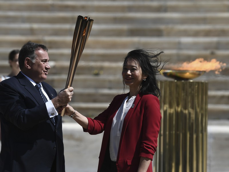 Na snímke vľavo s olympijskou pochodňou prezident Gréckeho olympijského výboru Spyros Kapralo, vpravo bývalá japonská plavkyňa Imoto Naoková počas jej slávnostného odovzdania pre letné olympijské hry 2020 v Tokiu